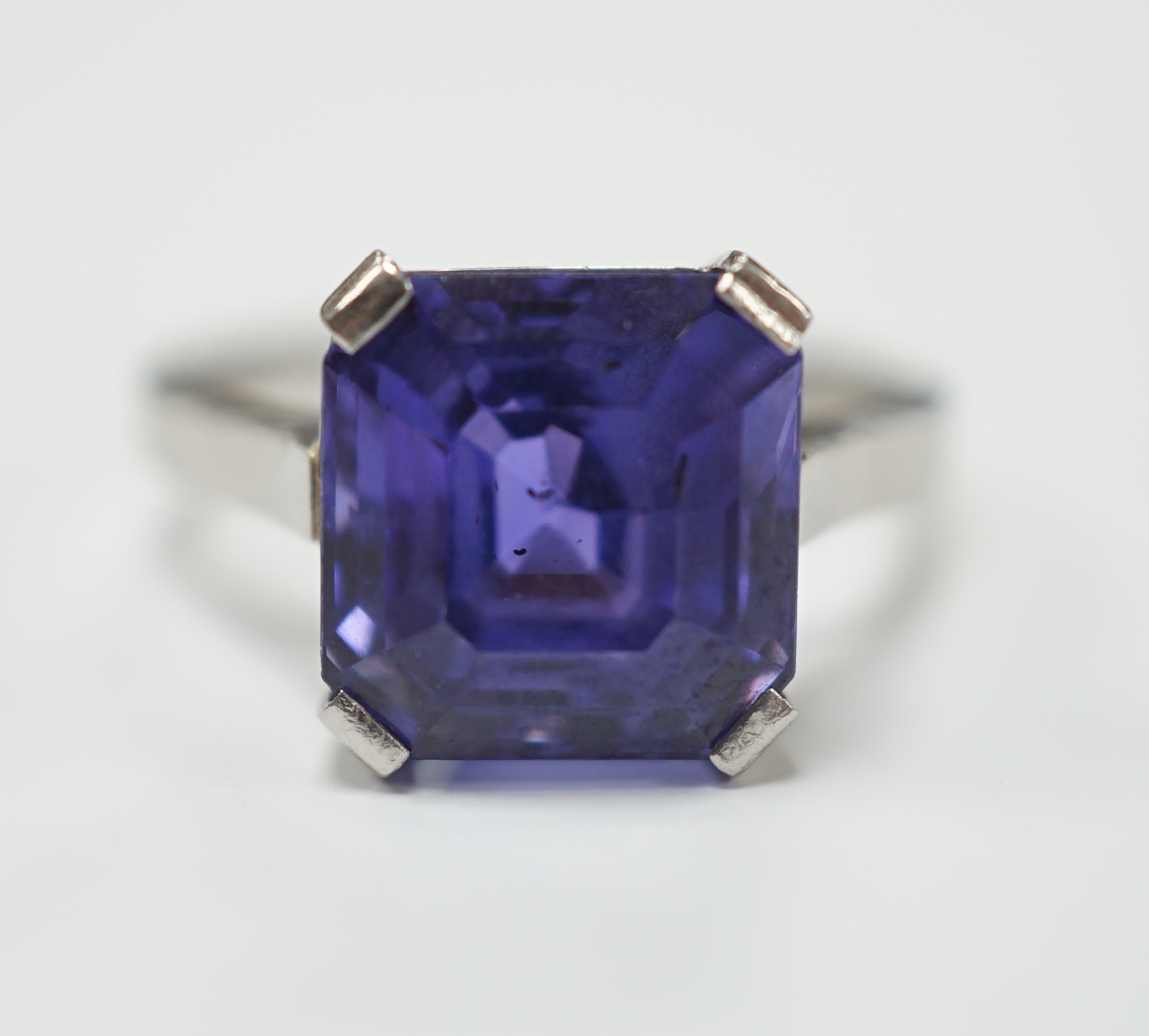 A white metal and single stone and square cut blueish purple sapphire set dress ring, size M, gross weight 5.6 grams, the stone measuring 10mm by 9,8mm, with a depth of 7.4mm.